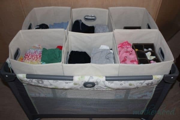 A clothes organizer for baby or toddler clothes made from a play yard with the bassinet feature in along with 6 fabric storage bins sitting in the pack n play, with additional organizers for socks nested inside.