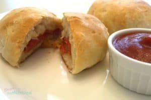 Image is of one of the kid friendly lunch ideas on this list, pizza pockets. Pockets are comprised of pepperoni and mozzarella stuffed inside a biscuit and baked, with a side of pizza sauce on a white plate.