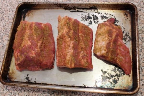 Seasoned rib slab cut into three portions on baking sheet