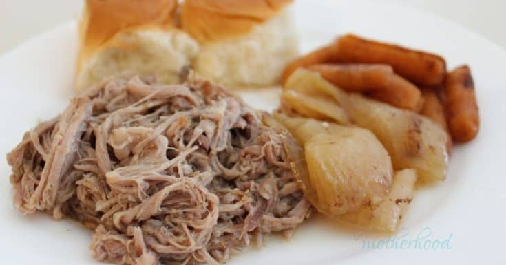 White plate with a helping of easy crock pot pulled pork, including baby carrots and onions cooked with it, and two hawaiian rolls.