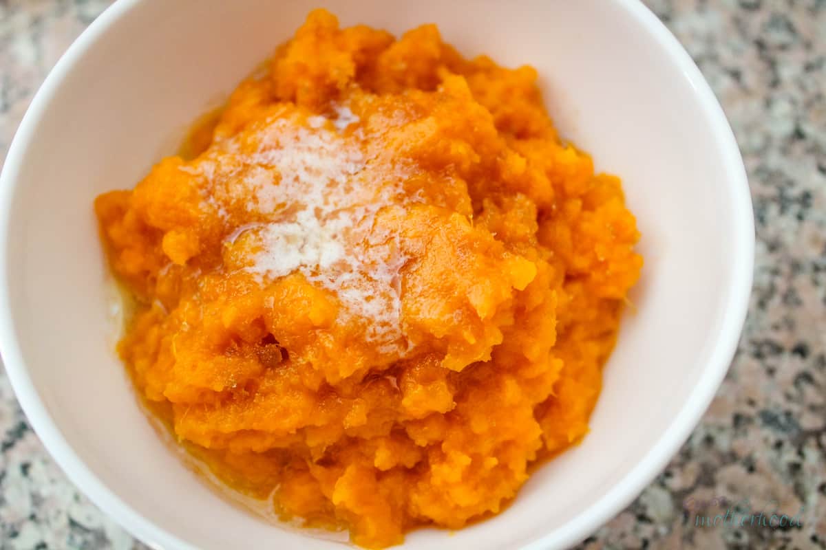 A white bowl filled with crock pot sweet potatoes and topped with butter that is melting.