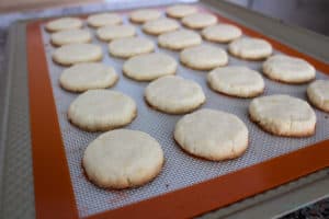 Baked cookies on silicone mat on cookie tray. Photo illustrates browning on the outer bottom edges of the cookies to indicate doneness.