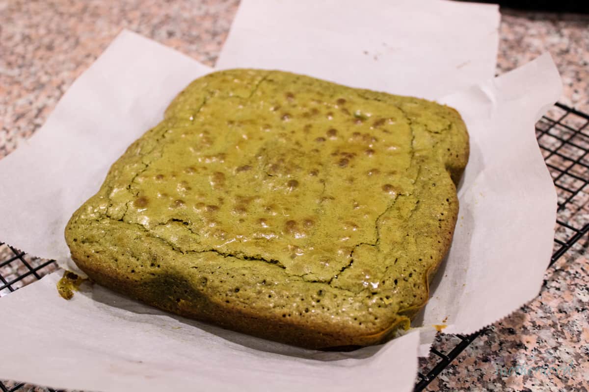 Baked uncut matcha brownies with parchment paper and cooling rack below it.